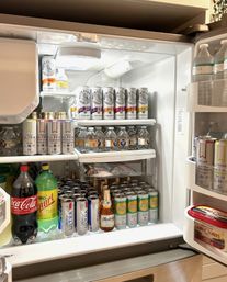 Open home refrigerator neatly stocked with rows of hard seltzer and canned cocktails, bottled water, soda bottles, a single beer bottle and a tub of butter on the door.