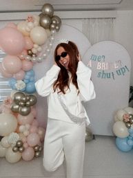 Smiling woman in white wearing a tiara and sash at an indoor bridal shower/bachelorette party with pastel pink, blue and gold balloon arch and a playful backdrop reading me? a bride? shut up!
