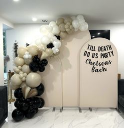 Neutral-toned beige, black and white balloon arch with pampas grass draped over a three-panel arched backdrop reading "Till Death Do Us Party" for a bachelorette celebration in a modern indoor space.