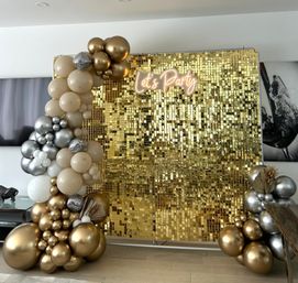 Gold sequin photo booth backdrop with beige, metallic gold and silver balloon garlands, disco-ball accents and a neon 'Let's Party' sign — chic indoor celebration display.