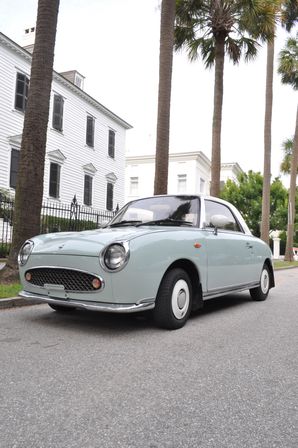 Mint-green vintage compact coupe parked on a palm-lined historic street in front of white colonial-style houses.