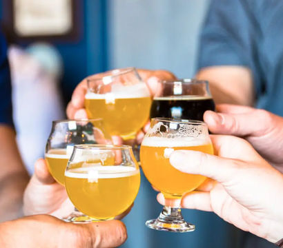 Close-up of five hands clinking small tulip beer glasses filled with pale golden and dark craft brews, a lively craft beer tasting toast at a local brewery.