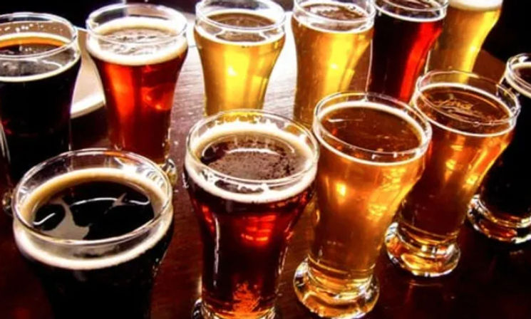 Craft beer flight of assorted small tasting glasses filled with pale golden, amber, and dark brews arranged on a wooden table, ready for a tasting.