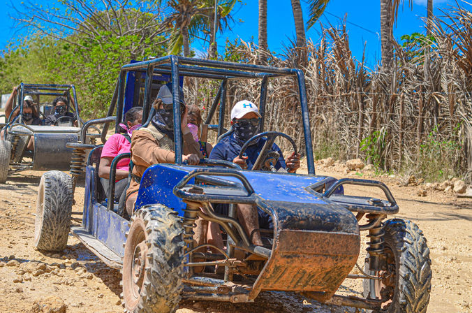 Dune buggy tour: group of riders wearing bandanas on blue buggies driving a tropical off-road dirt trail lined with palm trees under a bright blue sky
