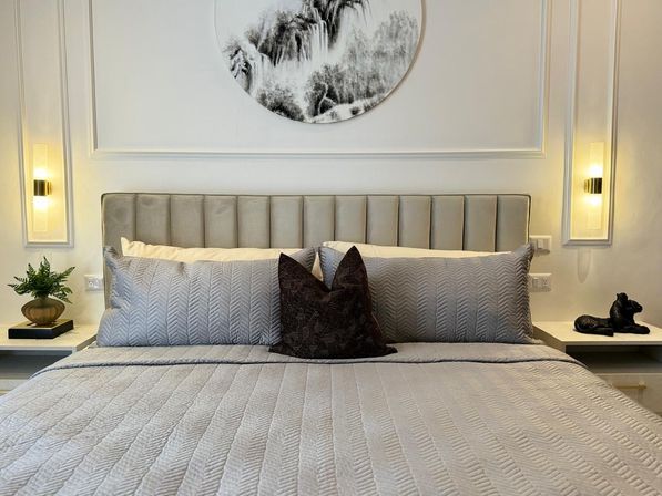 Cozy modern bedroom with king bed, gray quilted bedding and tufted headboard, round black-and-white wall art, warm wall sconces and styled bedside decor