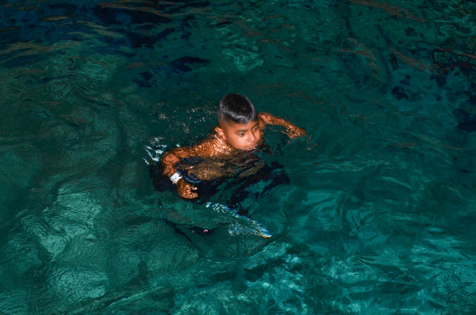 Young swimmer paddling in clear turquoise pool water with gentle ripples