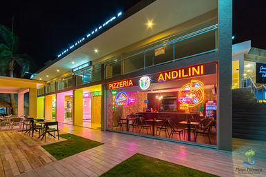 Neon-lit pizzeria storefront with indoor tables and outdoor patio seating in a modern tropical beachfront plaza at night