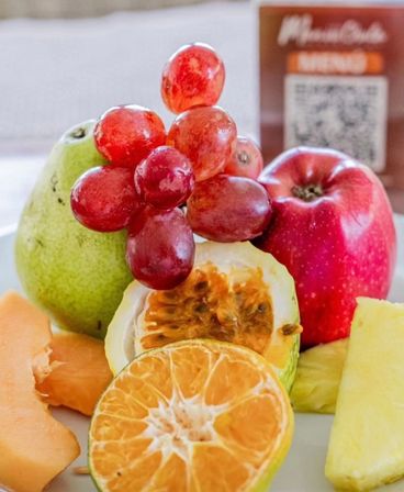 Close-up of a fresh fruit plate with red grapes atop a pear and red apple, halved passionfruit, sliced mandarin, cantaloupe and pineapple