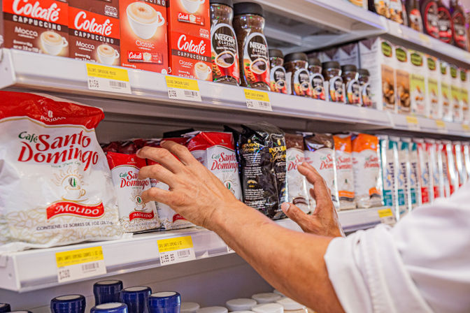 Hands reaching for colorful bags of ground coffee and jars of instant coffee on a grocery store coffee aisle shelf
