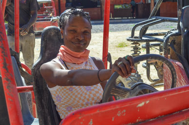 Smiling woman behind the wheel of a red off-road dune buggy on a sunny sandy track, hands on the steering wheel ready for outdoor adventure.