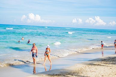 Tropical beach scene with turquoise ocean, blue sky and fluffy clouds, swimmers and beachgoers strolling along the wet sandy shoreline.