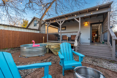 Cozy small backyard patio with covered wooden deck and steps, string lights, turquoise Adirondack chairs, and a galvanized stock-tank pool with a pink flamingo float