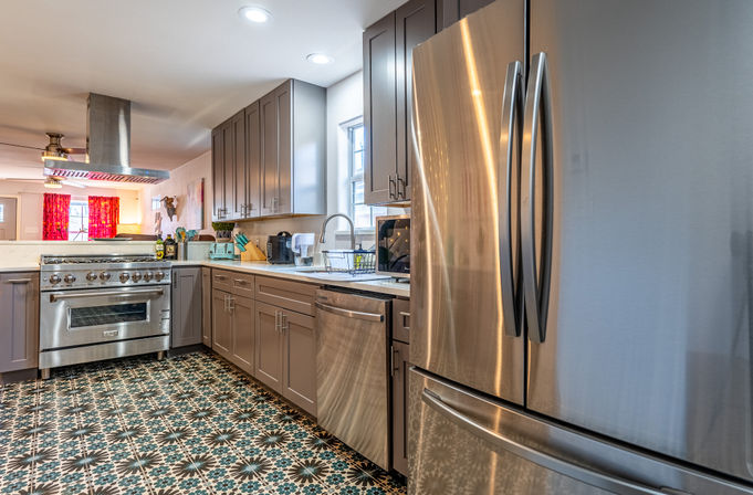 Bright modern kitchen with stainless-steel French-door refrigerator, professional gas range, gray shaker cabinets, farmhouse sink and bold patterned tile floor.