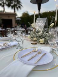 Elegant outdoor wedding reception table at dusk with gold-rimmed charger, white plate, gold flatware, glassware, taper candles, baby's breath and white roses, acrylic Table 10 sign.