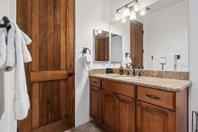 Cozy residential bathroom with rustic wooden door, granite countertop vanity, warm wood cabinets, oil-rubbed bronze faucets, large mirror and white towels