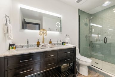 Spa-like modern bathroom with dark wood double-sink vanity and marble countertop, LED-lit mirror, and walk-in glass shower with seafoam green subway tile.