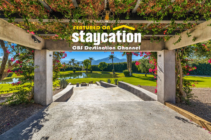 Sunny pergola patio draped in vines and bougainvillea, steps leading down to a pond, palm-tree lawn and distant mountain view