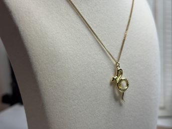 Gold snake pendant necklace with small sparkling stones displayed on a white felt bust — close-up jewelry product shot