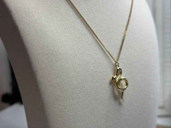 Gold snake pendant necklace with small sparkling stones displayed on a white felt bust — close-up jewelry product shot