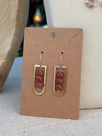 Handmade boho dangle earrings on a kraft display card — gold-tone U-shaped brass frames with three stacked earthy red beads and simple gold hooks.