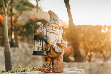 Cheerful garden gnome statue holding a lantern and shovel on a stone wall in a sunlit garden at golden hour