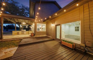 Cozy residential backyard wood deck at dusk with string lights, covered outdoor kitchen/grill and large window into the home