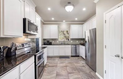 Bright modern U-shaped kitchen with white cabinets, dark granite counters, stainless steel appliances, tile floor, recessed lighting and window over the sink.