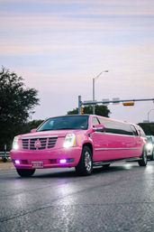 Bright pink Cadillac stretch limousine cruising on an urban street at dusk, headlights glowing and chrome wheels shining — vibrant party limo scene.
