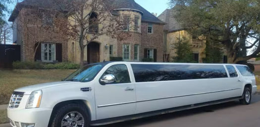 White Cadillac Escalade stretch limousine parked on a suburban street in front of a large brick mansion with oak trees and a manicured lawn