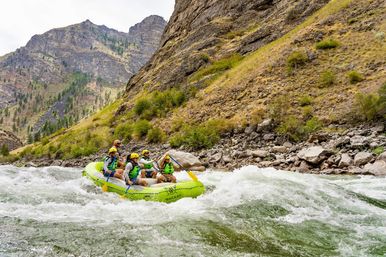 Group whitewater rafters in a bright inflatable raft paddling through rapids in a rocky mountain river canyon — outdoor adventure with helmets and life jackets