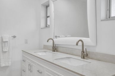 Bright modern white bathroom vanity with double undermount sinks, marble countertop, brushed-nickel faucets and large framed mirror