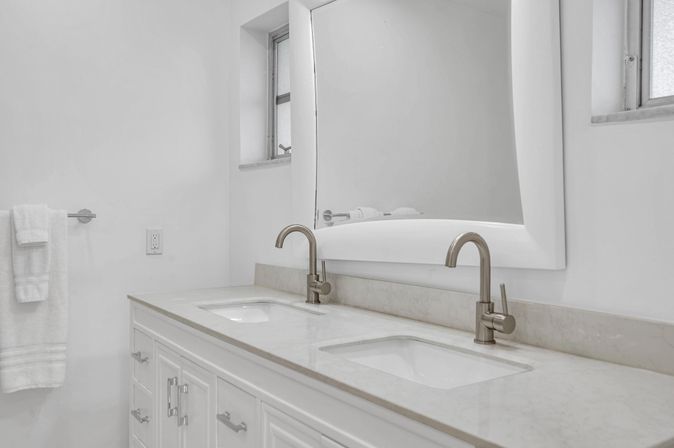 Bright modern white bathroom vanity with double undermount sinks, marble countertop, brushed-nickel faucets and large framed mirror