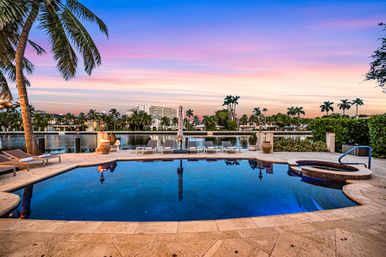 Waterfront tropical pool and spa at sunset — palm trees, lounge chairs and a pastel sky reflecting in the calm canal for a luxurious coastal backyard vibe.