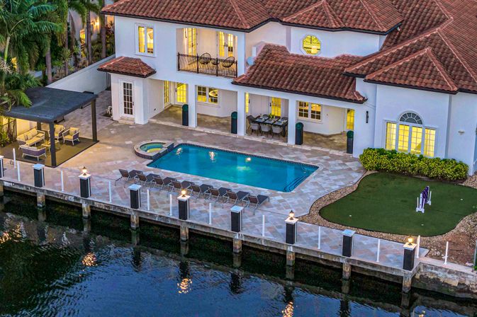 Canal-front Mediterranean villa at dusk with red-tile roof, lit patio, swimming pool and spa, pergola lounge, sunbeds and private dock
