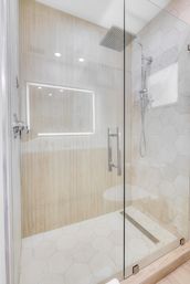 Modern spa-like walk-in shower with frameless glass door, overhead rain shower, hexagon stone tiles and light wood accent wall