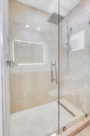 Modern spa-like walk-in shower with frameless glass door, overhead rain shower, hexagon stone tiles and light wood accent wall
