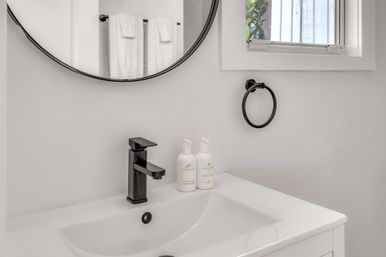 Minimalist white bathroom vanity with matte-black faucet and towel ring, round mirror reflecting folded white towels and a small window with natural light.
