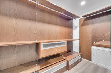 Modern walk-in closet with custom dark wood shelving, floating drawers, mesh-front cabinets and recessed ceiling light.