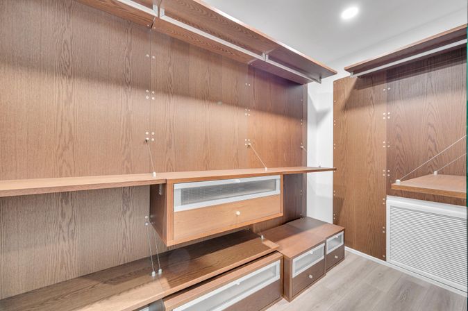 Modern walk-in closet with custom dark wood shelving, floating drawers, mesh-front cabinets and recessed ceiling light.