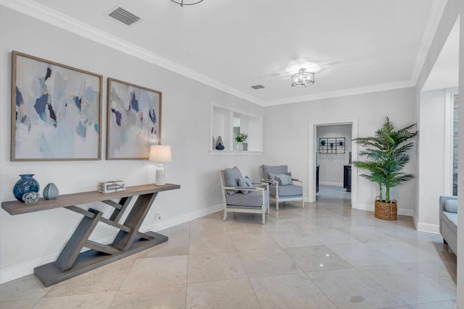 Modern airy foyer with marble tile floor, light-gray walls, wooden console table beneath abstract art, two cushioned armchairs and a potted palm