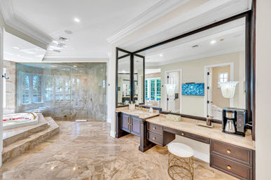 Spa-like luxury master bathroom with glossy marble floors, glass-enclosed walk-in shower, sunlit soaking tub with rose petals, dark wood double vanity and oversized mirror.