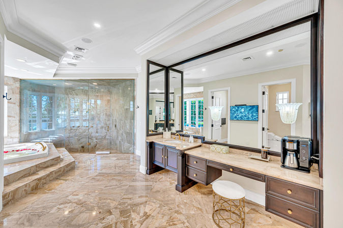 Spa-like luxury master bathroom with glossy marble floors, glass-enclosed walk-in shower, sunlit soaking tub with rose petals, dark wood double vanity and oversized mirror.