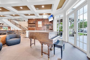 Antique grand piano in a bright luxury lounge with bar, coffered ceiling and French doors opening to a palm-lined patio