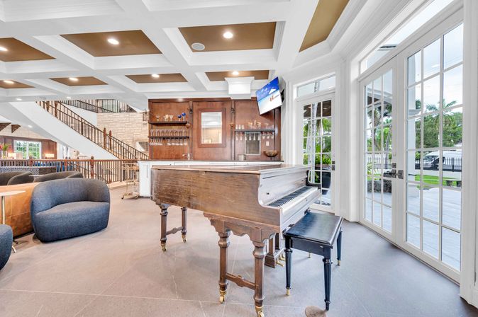 Antique grand piano in a bright luxury lounge with bar, coffered ceiling and French doors opening to a palm-lined patio