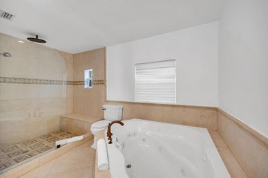 Spa-like master bathroom with jetted soaking tub, bronze faucet, glass walk-in shower and beige marble tile.