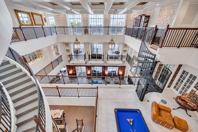 Bright multi-level atrium with iron spiral staircase, open balconies, blue pool table, leather lounge and tall windows with stone accent walls.