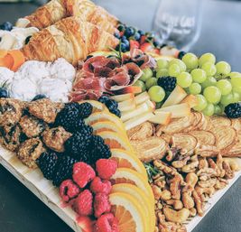 Gourmet charcuterie board with flaky croissants, prosciutto, sliced cheeses, green grapes, berries and mixed nuts