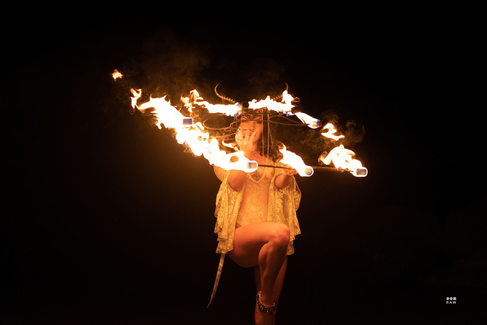 Fire performer balancing on one leg while twirling a flaming hoop and torches in a dramatic nighttime show