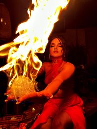 Woman in red dress performing an indoor fire act, holding a blazing orb with dramatic warm lighting