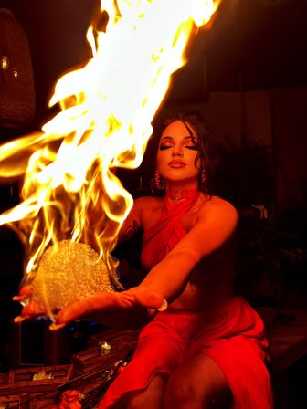 Woman in red dress performing an indoor fire act, holding a blazing orb with dramatic warm lighting